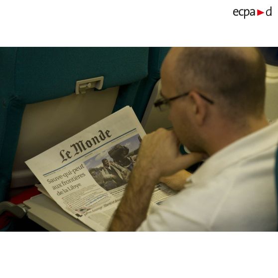 Un ressortissant évacué de Tripoli (Libye) lit un article sur le "Sauve-qui-peut aux frontières libyennes" en une du journal "Le Monde" dans l'avion Airbus A340 de l'escadron de transport 3/60 Esterel.