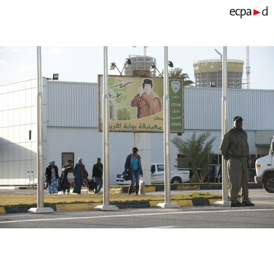 Des ressortissants évacués se dirigent vers leur avion pour l'embarquement sur l'aéroport de Tripoli (Libye), passant près d'une affiche représentant le colonel Kadhafi.