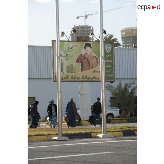 Des ressortissants évacués se dirigent vers leur avion pour l'embarquement sur l'aéroport de Tripoli (Libye), passant près d'une affiche représentant le colonel Kadhafi.