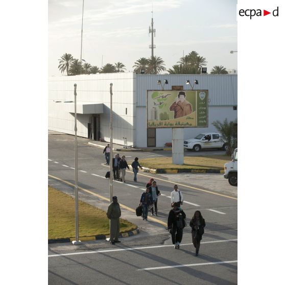 Des ressortissants évacués se dirigent vers leur avion pour l'embarquement sur l'aéroport de Tripoli (Libye), passant près d'une affiche représentant le colonel Kadhafi.