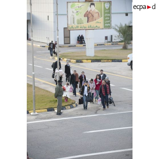 Des ressortissants évacués se dirigent vers leur avion pour l'embarquement sur l'aéroport de Tripoli (Libye), passant près d'une affiche représentant le colonel Kadhafi.