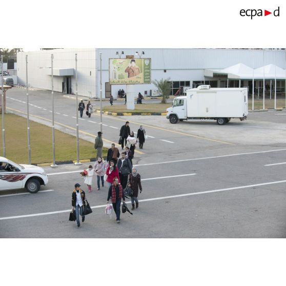 Des ressortissants évacués se dirigent vers leur avion pour l'embarquement sur l'aéroport de Tripoli (Libye), passant près d'une affiche représentant le colonel Kadhafi.