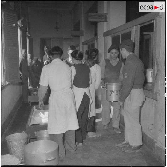 Du personnel vitenamien s'occupe de récipients remplis d'aliments dans un couloir à l'hôpital militaire Lanessan.