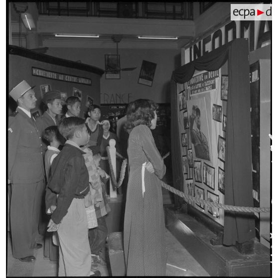 Groupe de civil et de militaires devant un panneau d'information annonçant la mort du maréchal de Lattre de Tassigny dans un hall du Service d'information.