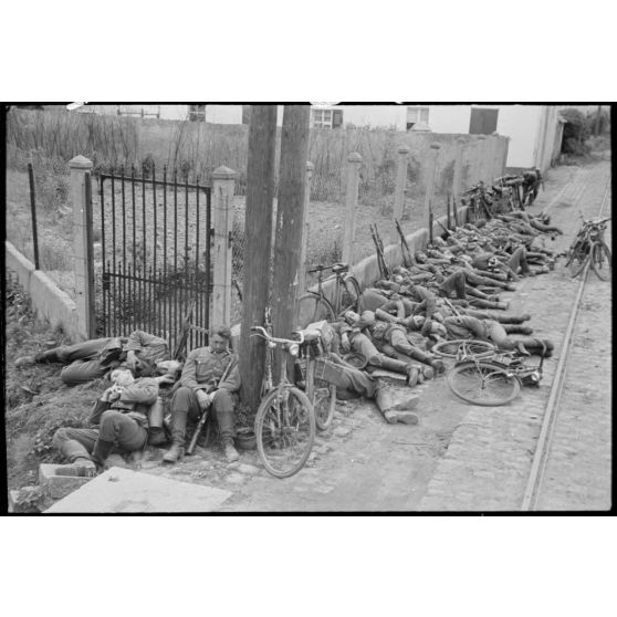 En Belgique, entre Mons et Valenciennes et à quelques kilomètres de Thulin, des cyclistes allemands prennent du repos dans la rue de Villiers à Hensies.