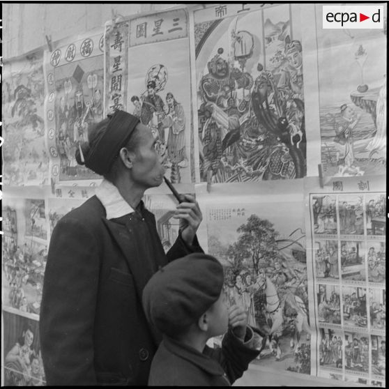 Un homme et un enfant devant des estampes chinoises de Hong Kong.