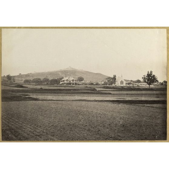 [Chine, 1870-1890. Vue d'une plaine avec des bâtiments de style colonial dont une église. A l'arrière-plan, sur une colline, un ouvrage fortifié].