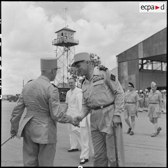 Le général Navarre, commandant en chef en Indochine, est accueilli par le général Cogny, commandant en chef des FTNV (forces terrestres du Nord-Vietnam), avec qui il échange des salutations sur l'aérodrome de Bach Mai.