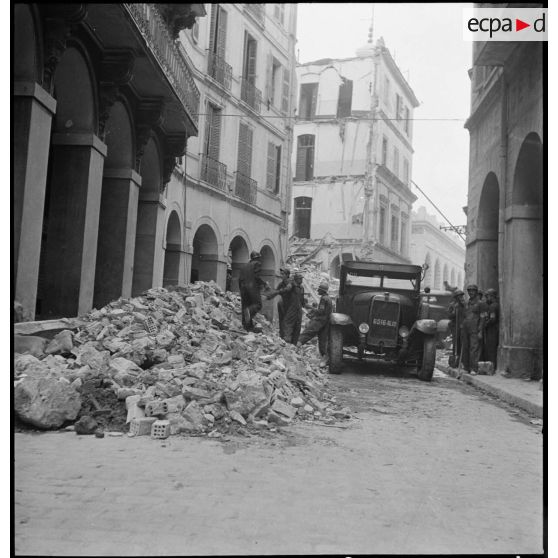 Suite au bombardement allemand de la nuit du 18 au 19 avril 1943, des volontaires de la défense passive déblaient des gravats dans une rue donnant sur la place du Gouvernement à Alger.