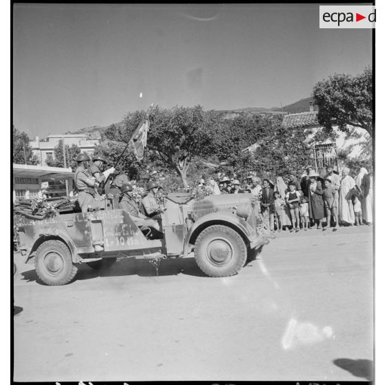 Un véhicule de liaison allemand Kfz-15 pris à l'ennemi par le 65e RAA (régiment d'artillerie d'Afrique) pendant la campagne de Tunisie, à bord duquel l'étendard du régiment est embarqué, défile dans une rue de Blida.