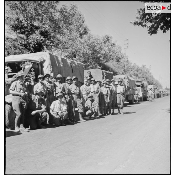 Portrait de groupe d'artilleurs du 65e RAA (régiment d'artillerie d'Afrique), de retour de la campagne de Tunisie, posant devant une colonne de véhicules sur une route menant à Blida.