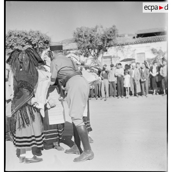 De retour de la campagne de Tunisie, le colonel Dumas, commandant le 65e RAA (régiment d'artillerie d'Afrique), embrassent des jeunes filles portant les costumes traditionnels alscien et lorrain.