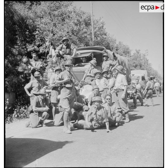 Portrait de groupe d'artilleurs du 65e RAA (régiment d'artillerie d'Afrique), de retour de la campagne de Tunisie, posant devant une colonne de véhicules sur une route menant à Blida.