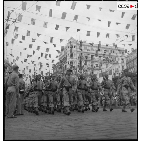 Défilé de tirailleurs du 1er RTA (régiment de tirailleurs algériens) lors du 14 juillet 1943 dans une rue pavoisée de la ville.