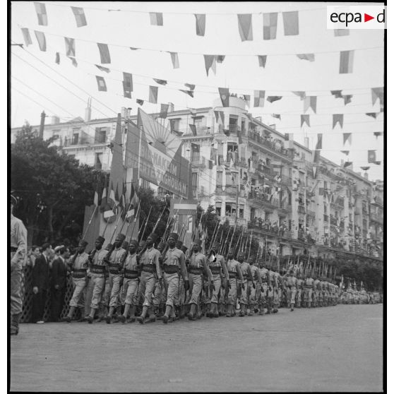 Défilé de tirailleurs du 19e RTS (régiment de tirailleurs sénégalais) (sous réserves), unité en garnison à Alger lors du 14 juillet 1943. Ils portent la tenue française avec écusson tricolore frappé de l'ancre de marine sur la poitrine.