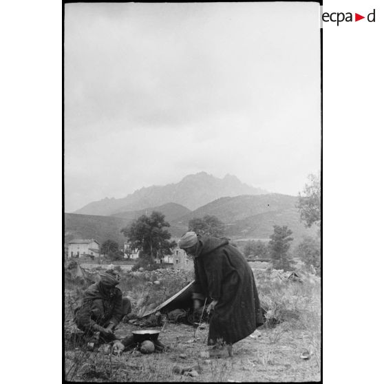 Des goumiers d'un goum du 2e GTM (groupe de tabors marocains) se préparent un repas au bivouac. A l'arrière-plan, le col de Teghime.