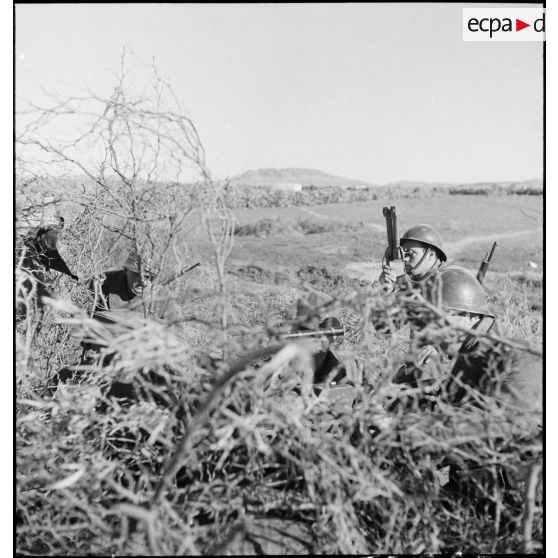 Des servants d'un canon antichar américain de 37 mm sont camouflés dans la végétation pendant que le chef de pièce observe l'objectif avec des jumelles périscopiques.