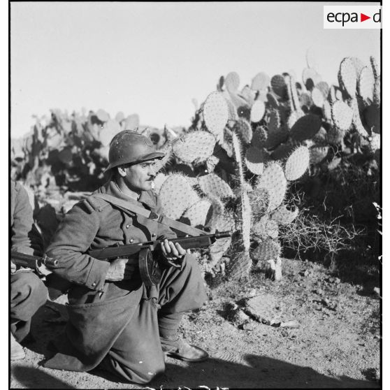 Tirailleur du 9e RTA (régiment de tirailleurs algériens) de la DMC (Division de marche de Constantine) armé d'un pistolet-mitrailleur Thompson M1 avec chargeur circulaire, posté au milieu de cactus.