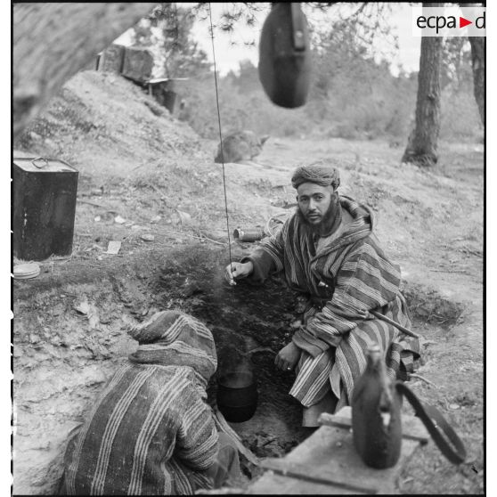 Des supplétifs du 1er GSM (groupe de supplétifs marocains) de la 1re DMM (division de marche du Maroc) chauffent une gamelle dans un trou individuel de combat.