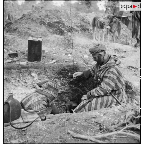 Des supplétifs du 1er GSM (groupe de supplétifs marocains) de la 1re DMM (division de marche du Maroc) chauffent une gamelle dans un trou individuel de combat.