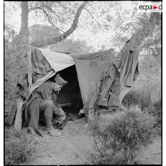 Un lieutenant d'un bataillon du 7e RTA (régiment de tirailleurs algériens) de la DMC (division de marche de Constantine) s'affaire à l'entrée de sa tente dans un campement.