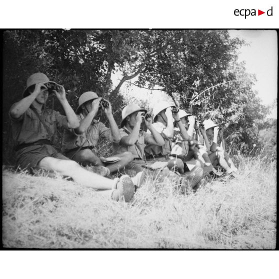 Lors d'une école à feu, des élèves aspirants de l'école de Cherchell observent à la jumelle les résultats d'un tir d'artillerie.