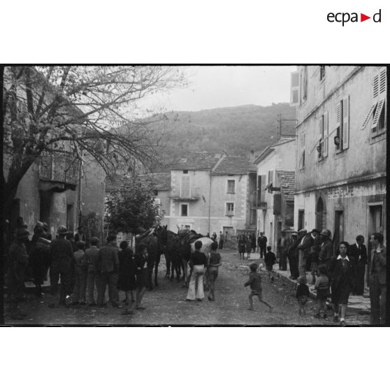 Des soldats français et italiens se trouvent dans une rue de la commune, au milieu de la population civile.