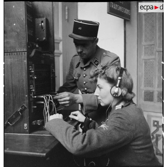 Portrait d'un lieutenant du corps féminin des transmissions utilisant un central téléphonique dans un centre de formation, sous le contrôle d'un instructeur masculin.