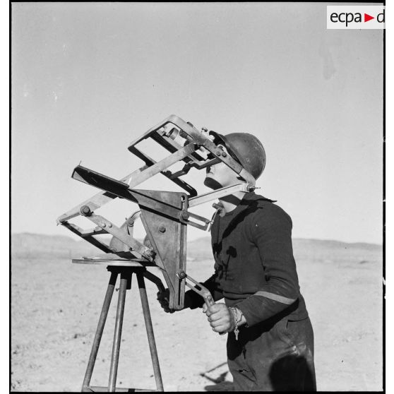 Un canonnier marin d'une batterie mobile de 90 de marine scrute le ciel avec des jumelles d'artillerie sur trépied.