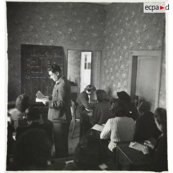 Un lieutenant du corps féminin des transmissions dispense un cours pratique d'enseignement du code Morse dans un centre de formation, sous le contrôle d'un instructeur masculin.