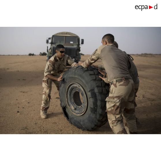 Des mécaniciens acheminent la roue crevée d'un VAB vers un camion GBC-180 lors d'une intervention technique dans le désert.