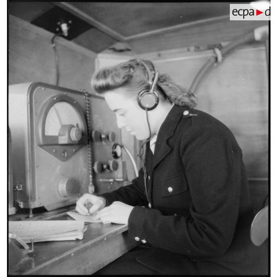 Instruction pratique de TSF dans une remorque d'écoute pour une élève de l'école des transmissions des personnels féminins de l'armée de l'Air : l'écoute en station, transcription d'un message.