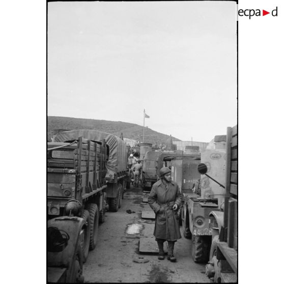 Un soldat marche entre les véhicules entreposés sur le pont d'un bâtiment de transport américain : half-track M3 et camions GMC.