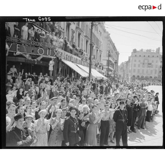 La population marseillaise acclame les troupes lors du défilé, à l'angle de la Canebière et du quai des Belges.