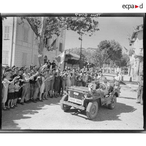 La foule acclame les opérateurs du service cinématographique de l'Armée (SCA) qui d'après la légende d'origine accompagnent la première patrouille américaine.