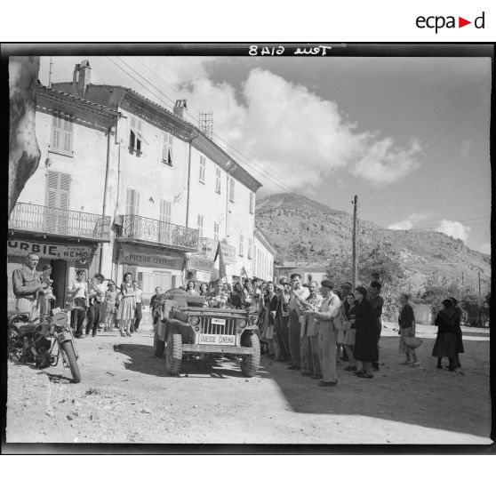 La foule acclame les opérateurs du service cinématographique de l'Armée (SCA) qui d'après la légende d'origine accompagnent la première patrouille américaine.