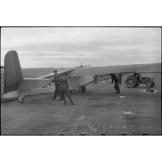 Sur la piste du terrain d'aviation, un tracteur agricole tracte le planeur DFS-230 du Luftlandegeschwader 1 (8./LLG 1) vers un nouvel emplacement.