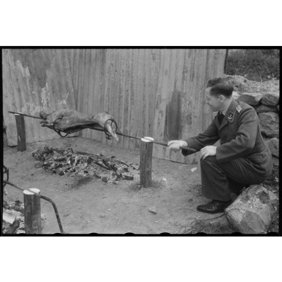 Un lieutenant d'un service administratif de la Luftwaffe surveille la cuisson de la viande lors d'un méchoui organisé au sein d'une unité de reconnaissance de l'armée de l'Air allemande (Aufklärungsgruppe).