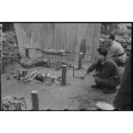 Des aviateurs de la Luftwaffe surveillent la cuisson de la viande pour méchoui organisé au sein d'une unité de reconnaissance de l'armée de l'Air allemande (Aufklärungsgruppe).