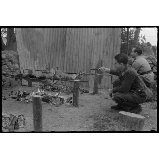 Des aviateurs de la Luftwaffe surveillent la cuisson de la viande pour méchoui organisé au sein d'une unité de reconnaissance de l'armée de l'Air allemande (Aufklärungsgruppe).