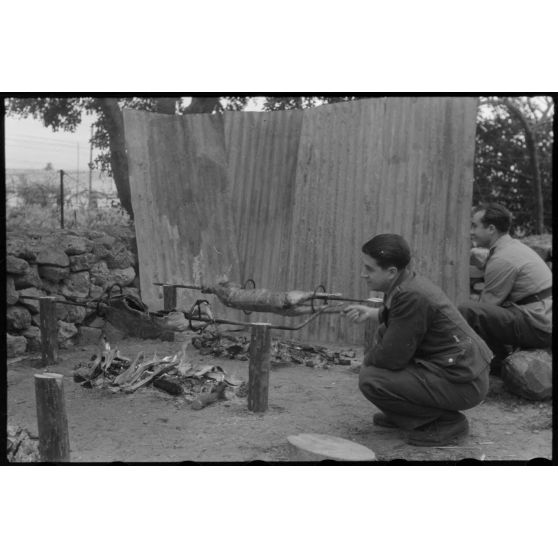 Des aviateurs de la Luftwaffe surveillent la cuisson de la viande pour méchoui organisé au sein d'une unité de reconnaissance de l'armée de l'Air allemande (Aufklärungsgruppe).