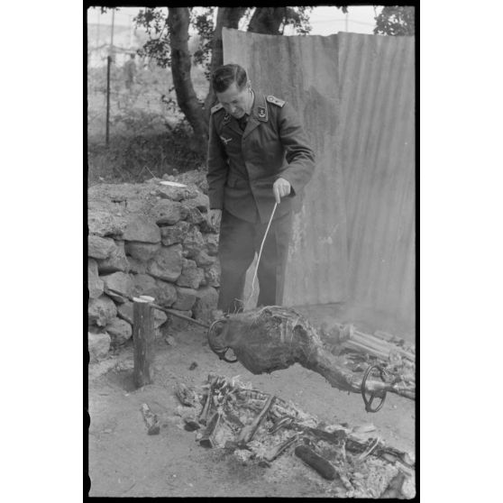 Un lieutenant d'un service administratif de la Luftwaffe surveille la cuisson de la viande lors d'un méchoui organisé au sein d'une unité de reconnaissance de l'armée de l'Air allemande (Aufklärungsgruppe).