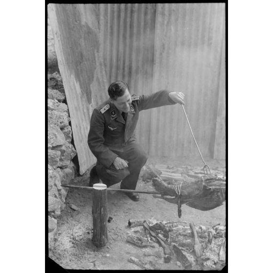 Un lieutenant d'un service administratif de la Luftwaffe surveille la cuisson de la viande lors d'un méchoui organisé au sein d'une unité de reconnaissance de l'armée de l'Air allemande (Aufklärungsgruppe).