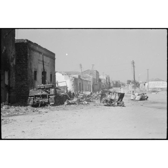 Destruction dans une ville aux alentours d'Augusta, une colonne de véhicules allemands a souffert des coups de l'artillerie ou de l'aviation alliée, les carcasses d'un semi-chenillé lourd et de voitures sont alignées le long des maisons du bourg.