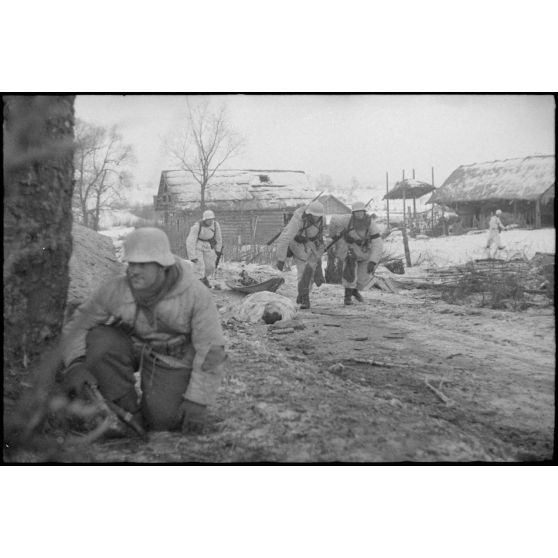 Non loin d'un village, durant la bataille de Witebsk, des fantassins allemands tirent une luge (traîneau) et passent devant le cadavre d'un soldat soviétique.