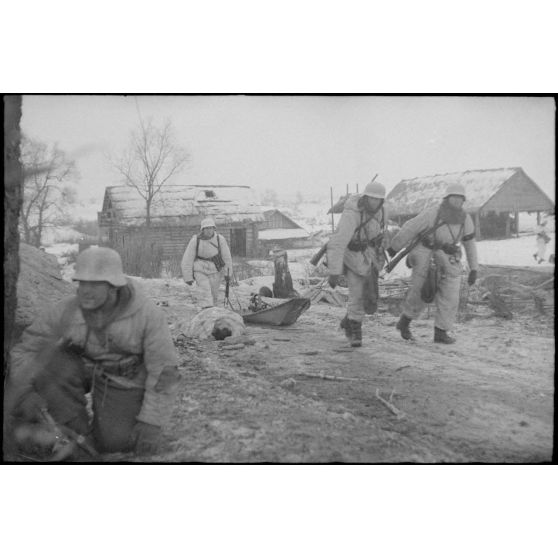 Non loin d'un village, durant la bataille de Witebsk, des fantassins allemands tirent une luge (traîneau) et passent devant le cadavre d'un soldat soviétique.