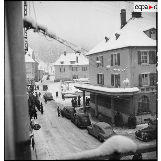 Vue en plongée d'une rue enneigée de Maîche avec les voitures des autorités civiles et militaires venues rendre visite à la 1re Armée au PC de la 9e DIC (division d'infanterie coloniale) installé au château de Montalembert.