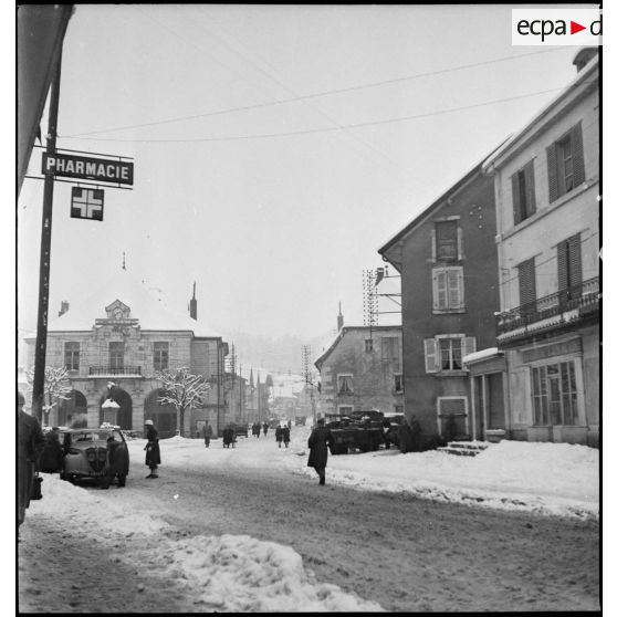 Vue en plongée d'une rue enneigée de Maîche avec les voitures des autorités civiles et militaires venues rendre visite à la 1re Armée au PC de la 9e DIC (Division d'infanterie coloniale) installé au château de Montalembert.