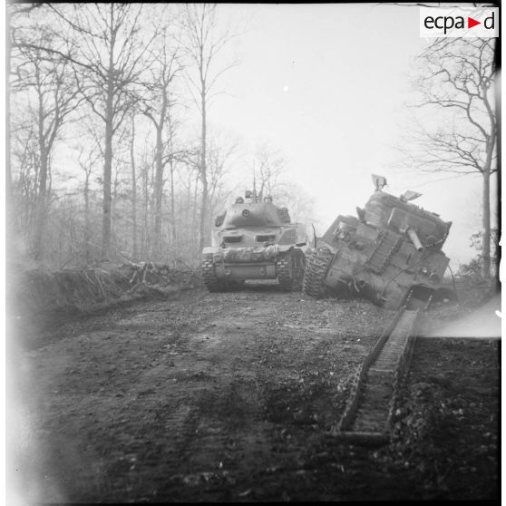 Un canon automoteur léger M8 HMC dépasse un char Sherman M4 endommagé vers Belfort.