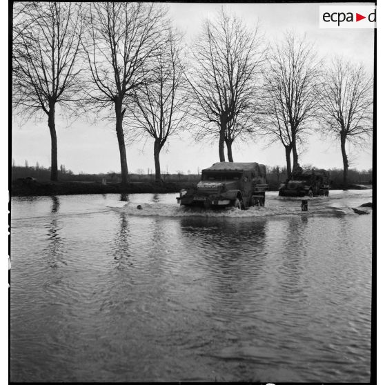 Des half-tracks du 64e RADB traversent une zone inondée aux abords de l'Ill.